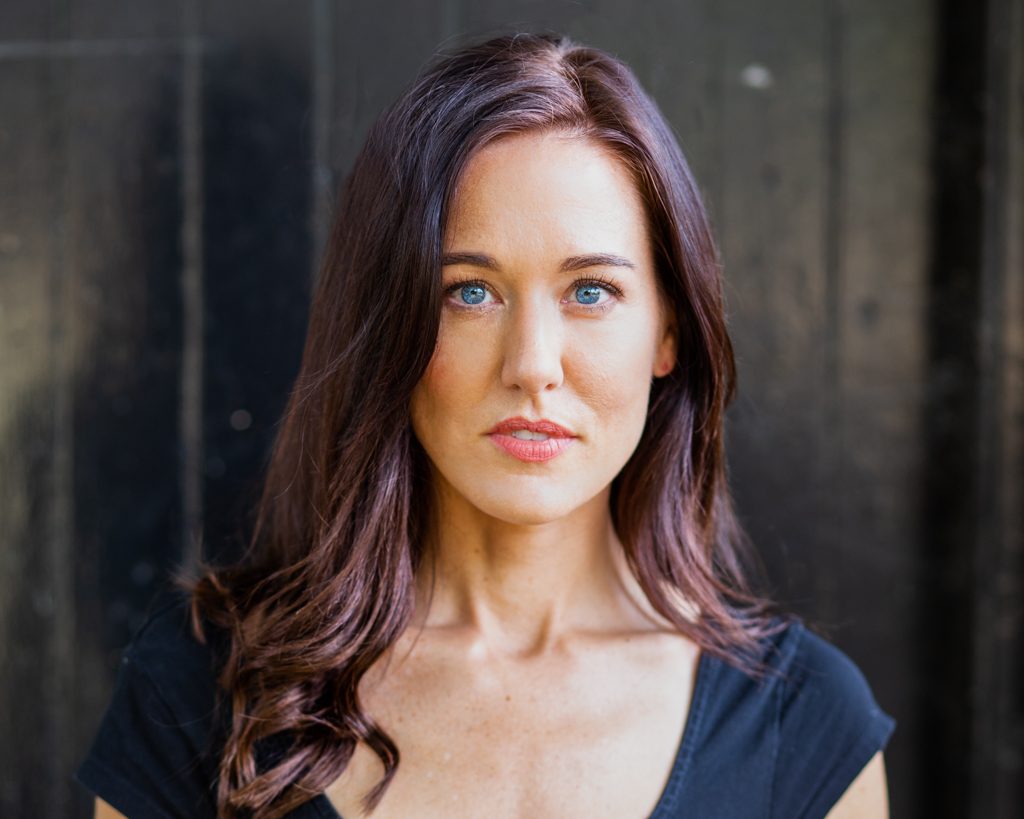 Actress with long dark hair and blue yes standing in front of door