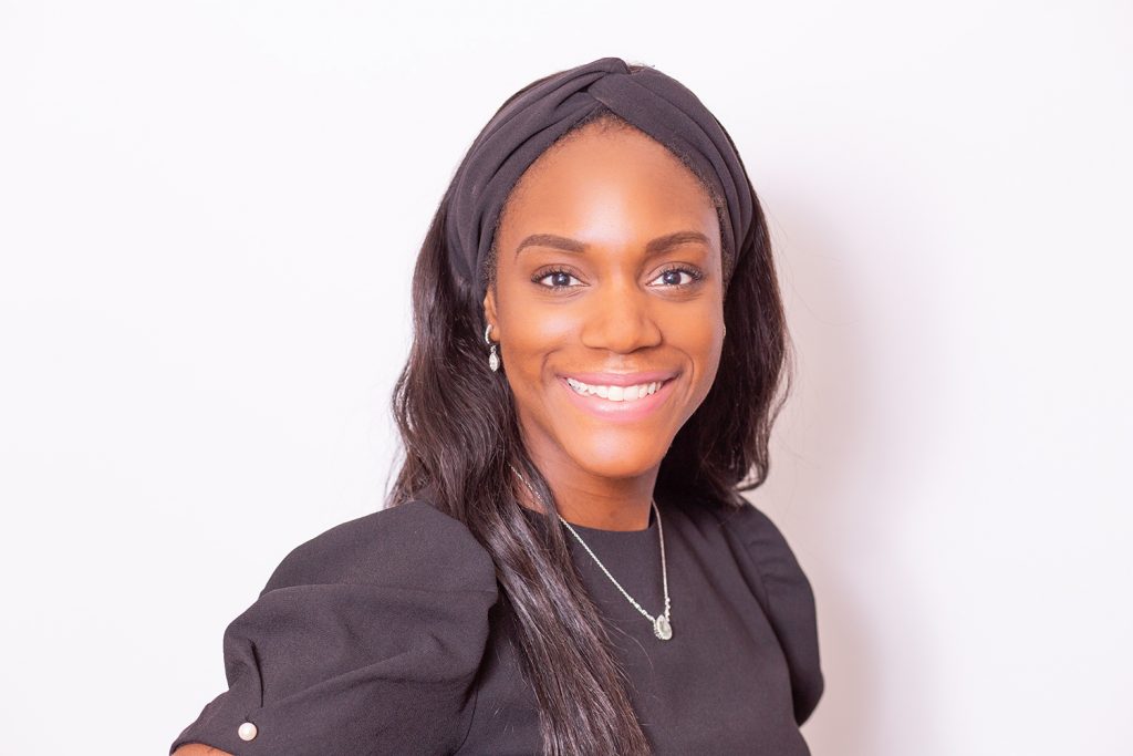 Pretty girl wearing black dress and black hairband smiling broadly into the camera with white background