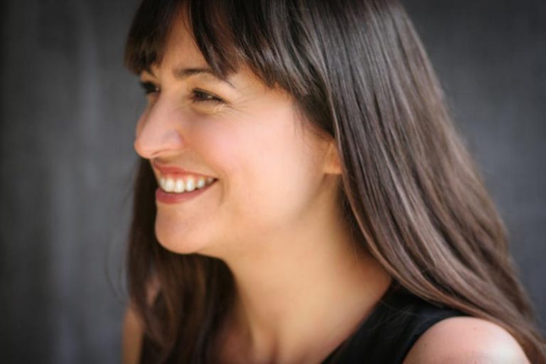 Woman smiling off camera with brown hair and black top