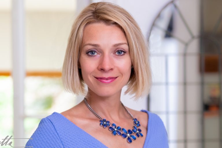 Smiling blonde woman with blue top and blue necklace