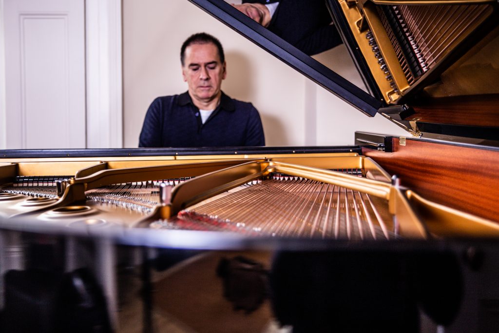 pianist sitting at piano with the piano lid open and in the foreground. Picture of the string of the piano and the interior