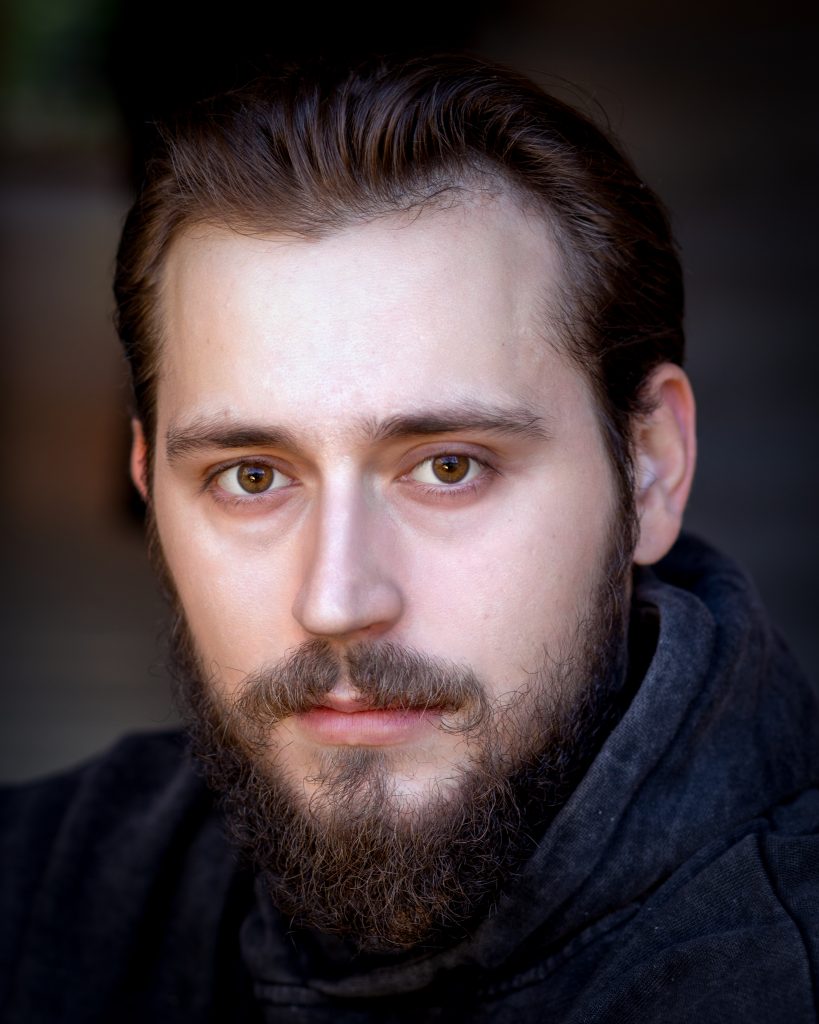 Actor with a curly black beard and dark grey top