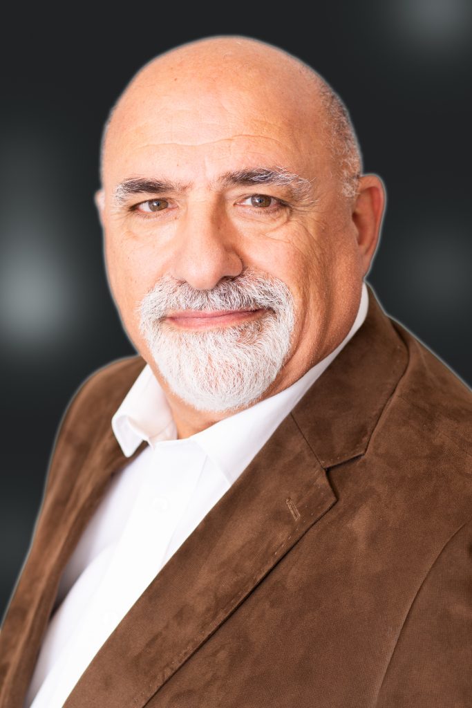 Distinguished looking bald older man with grey beard and wearing brown suede jacket. Looking into camera with black backdrop